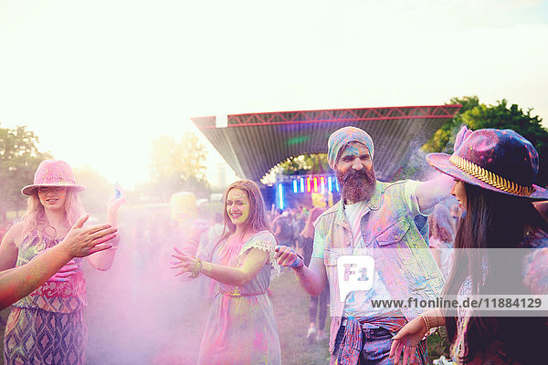 Young adult friends dancing and throwing coloured chalk powder at festival