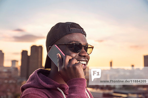 Junger Mann telefoniert mit seinem Smartphone auf einer Dachparty bei Sonnenuntergang in London  Großbritannien