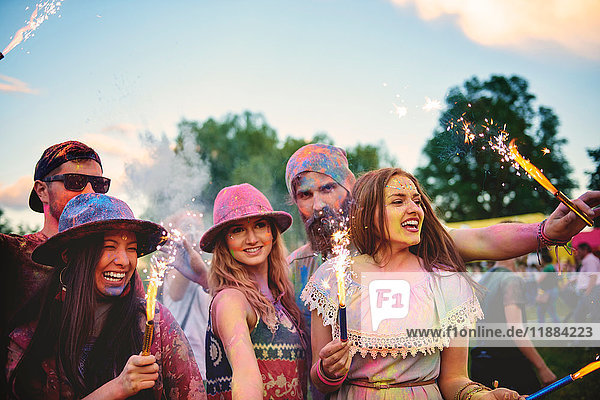 Young adults covered in coloured chalk powder dancing with sparklers at festival