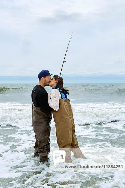 Young couple in waders kissing whilst sea fishing