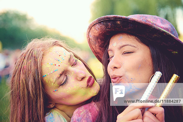 Portrait of two young women covered in coloured chalk powder puckering lips at festival