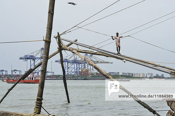 'Fisherman with chinese fishing nets with shipyard in background; Kochi  Kerala  India'