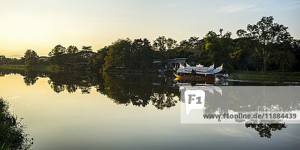 'Reflections in a tranquil river at sunset with a tour boat along the shoreline; Chiang Rai  Thailand'