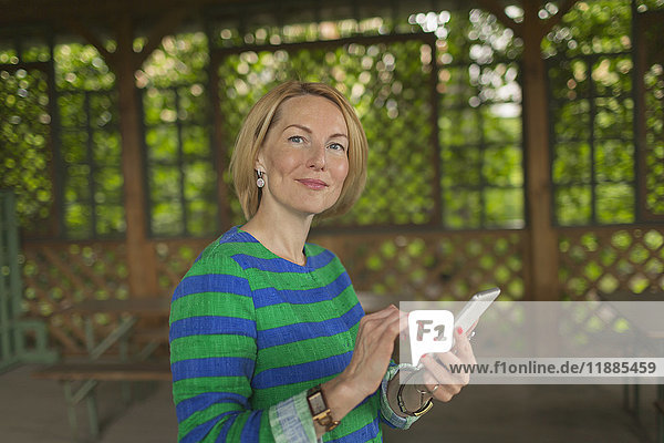 Porträt einer lächelnden Frau mit Smartphone im Pavillon im Park