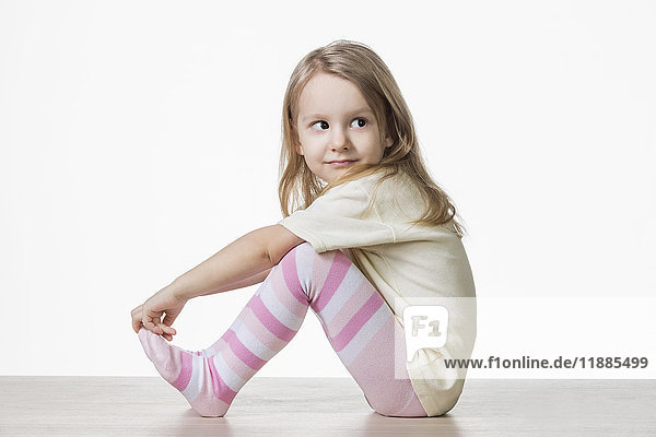 Side view of cute girl sitting on floor against white background
