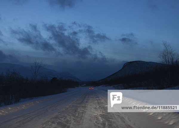 Fernansicht des Autos auf schneebedeckter Straße gegen den Himmel in der Dämmerung  Kiruna  Schweden