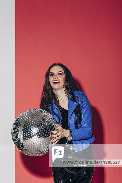 Portrait of happy beautiful woman holding disco ball against coral background