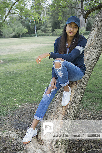 Portrait of young woman sitting on tree trunk at park