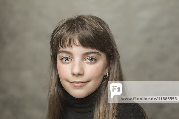 Porträt eines lächelnden Mädchens mit langen Haaren vor grauem Hintergrund