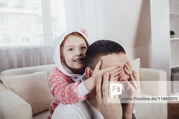Tochter  die Vaters Augen bedeckt  während sie zu Hause im Wohnzimmer spielt.