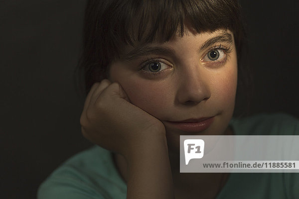 Porträt eines Mädchens  das mit der Hand auf dem Kinn auf grauem Hintergrund ruht.