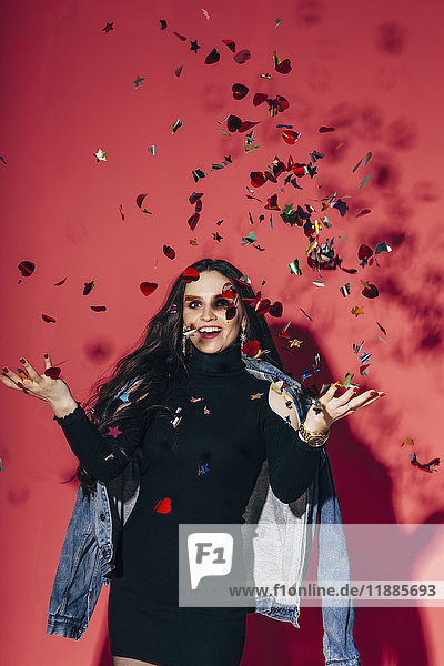 Portrait of happy young woman throwing confetti against coral background