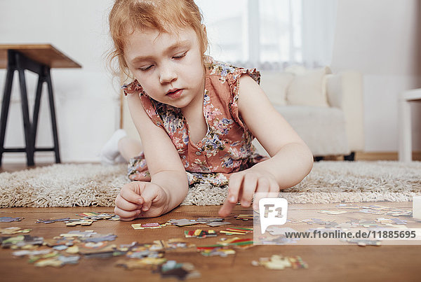 Mädchen spielt mit Puzzleteilen  während sie zu Hause auf dem Teppich liegt.
