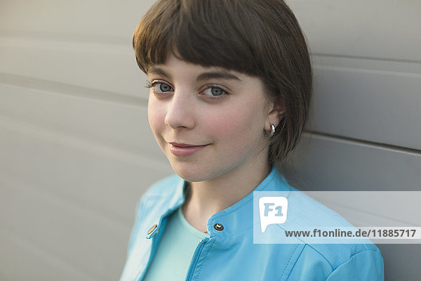 Close-up portrait of smiling girl wearing blue jacket leaning on white wall