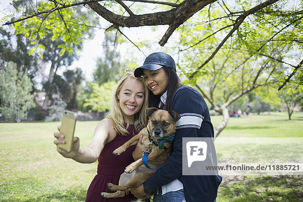 Lächelnde junge Frauen  die Selfie mit Hund im Park mitnehmen.