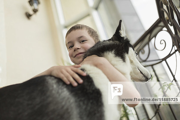 Niederwinkel-Porträt eines Jungen  der den Hund mit einem Geländer umarmt.