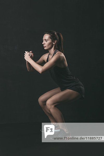 Full length of focused woman doing squat exercise against black background