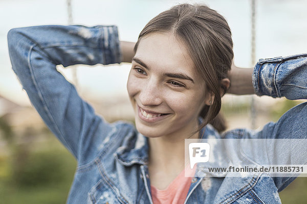 Lächelnde junge Frau bindet Haare beim Blick in den Park