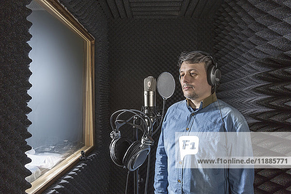 Musician standing by microphone with headphones in recording studio