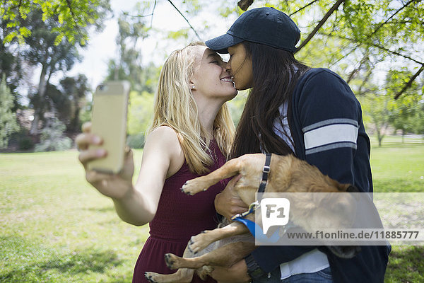 Frau  die sich küsst  während sie Selfie mit Hund im Park nimmt.