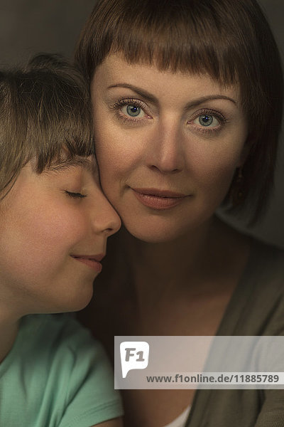 Porträt der lächelnden Mutter mit liebevoller Tochter vor grauem Hintergrund