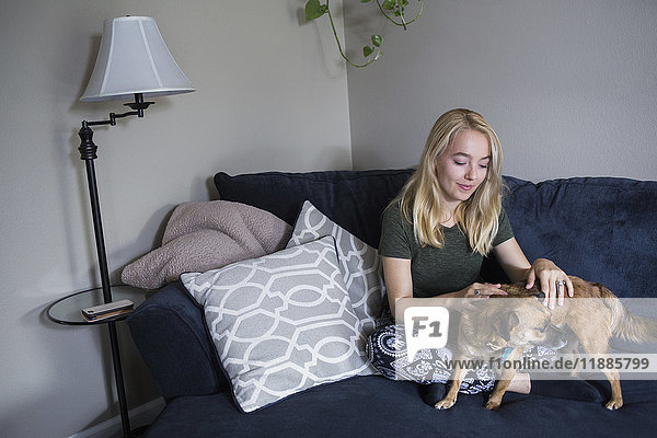 Junge blonde Frau sitzend mit Hund auf dem Sofa zu Hause