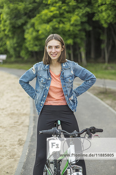 Lächelnde Frau mit Händen an der Hüfte auf dem Fahrrad auf der Straße sitzend