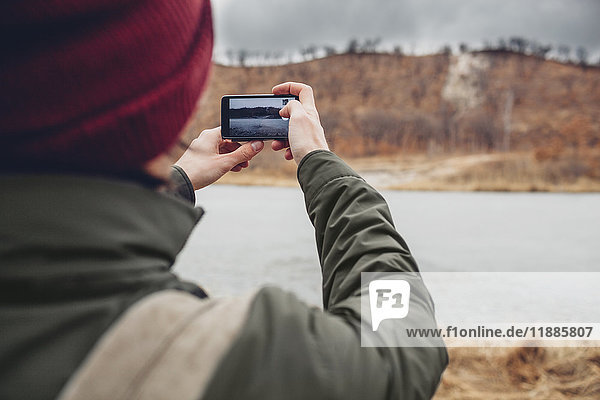 Rückansicht des Mannes  der den See durch ein Smartphone fotografiert  Blagoveschensk  Amur  Russland