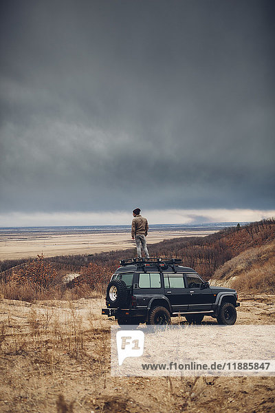 Distanzierter Mann steht auf einem Geländewagen über Land gegen bewölkten Himmel  Amur  Russland