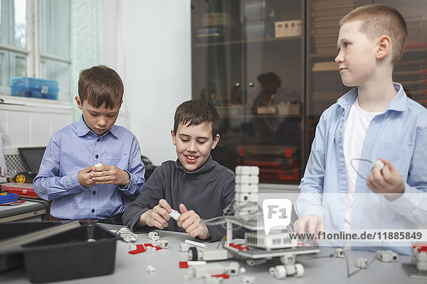 Lächelnde Schüler bei der Arbeit am Maschinenteil am Tisch im Klassenzimmer