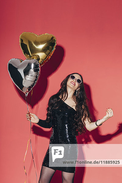 Happy young woman holding helium balloons against coral background