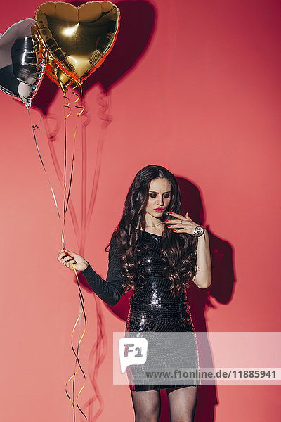 Fashionable woman holding helium balloons against coral background