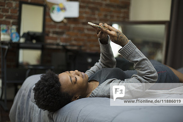 Junge Frau auf dem Bett liegend mit dem Handy zu Hause