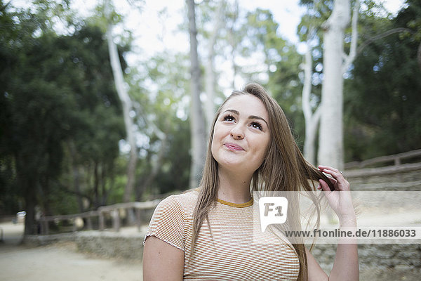 Nachdenkliche junge Frau spielt mit Haaren im Park