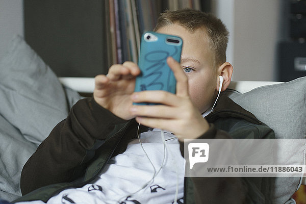 Junge hört Musik  während er zu Hause mit dem Smartphone telefoniert.