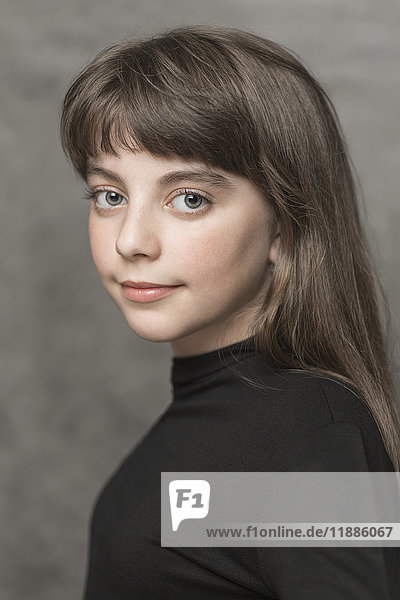 Seitenansicht Porträt eines lächelnden Mädchens mit langen Haaren vor grauem Hintergrund