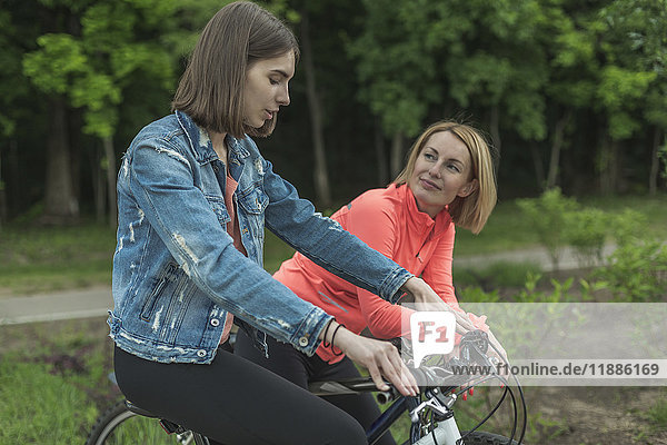 Lächelnde Mutter und Tochter beim Fahrradfahren im Park