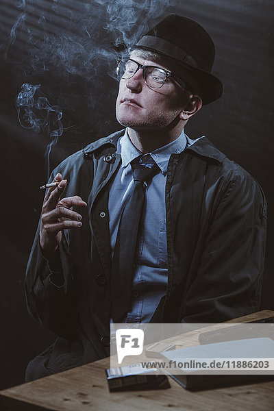 Young man sitting at table with gun while smoking cigarette