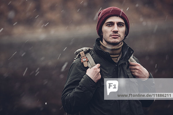 Portrait of man carrying backpack while standing outdoors during snowfall