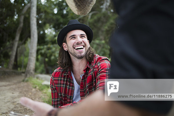 Fröhlicher Mann  der einen männlichen Freund ansieht  während er im Park sitzt.