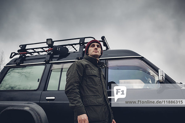 Low angle view of man standing by sports utility vehicle against cloudy sky