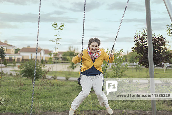 Happy senior woman swinging on swing at playground against sky