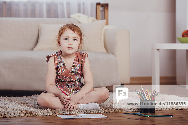 Portrait of smiling girl drawing while sitting on carpet in living room at home