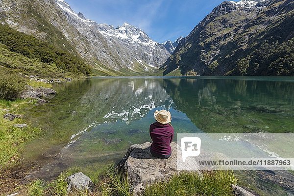 Weiblicher Wanderer mit Sonnenhut am Ufer sitzend  Lake Marian  Fiordland National Park  Te Anau  Southland  Südinsel  Neuseeland  Ozeanien
