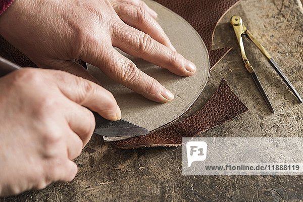 Schuhmacher  Hände schneiden mit Schablone und Messer ein Stück Leder auf Arbeitstisch  Kainisch  Steiermark  Österreich  Europa