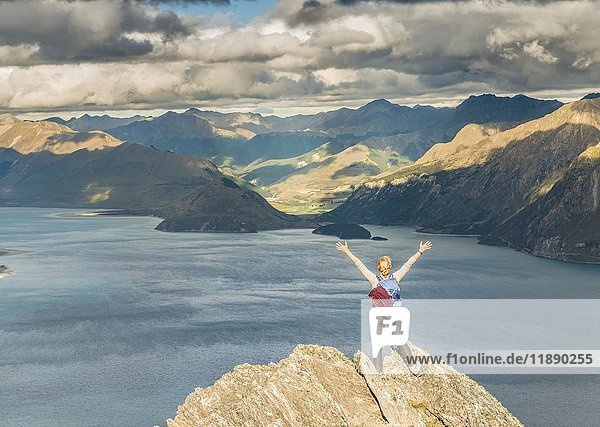 Female hiker on a rock  stretching arms in the air  Lake Hawea and mountain landscape  Isthmus Peak  Otago  South Island  New Zealand  Oceania