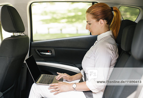 Businesswoman sitting on backseat of a car using laptop