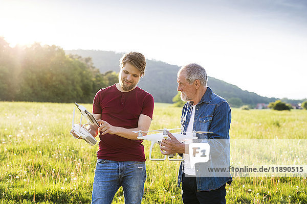 Senior father and his adult son with drone on a meadow