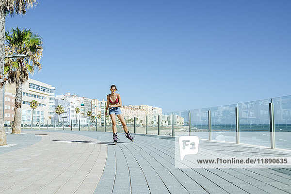 Junge Frau beim Inline-Skaten auf der Strandpromenade an der Küste