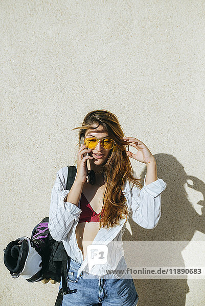 Junge Frau mit Inline-Skates in der Tasche spricht am Handy